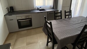 A compact kitchen with white cabinets, a built-in oven, and a dining area with a table and chairs. - Accommodation La Chaumière de Rambouillet 1-6 pers (Rambouillet)