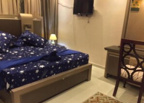 Relax in comfort with a bed featuring a star-patterned bedspread, a convenient table with a lamp, and a comfortable chair.