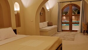 Un dormitori amb un llit gran, un sofà i vista a una piscina exterior a través d'una porta de vidre.