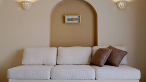Un sofà blanc amb tres coixins i una almoçada marró, col·locat sota un arc de la paret amb un quadre encimbellat.
