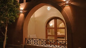 A room with a large arched doorway, a wooden door, and a small balcony with a railing.