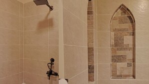 A bathroom with beige tiles, a showerhead, a towel rack, and a decorative arched window.