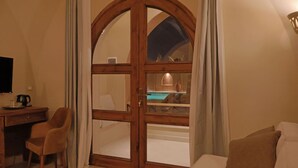 A room with a wooden door leading to a pool area, a desk with a chair, and a bed with pillows.