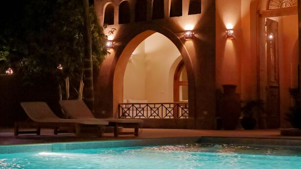 A pool area with lounge chairs and a building with arched windows and warm lighting.