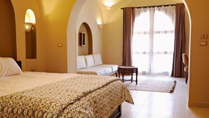 Camera d'albergo con un letto grande, un divano, un tavolino e vista sull'esterno tramite una finestra con tende.