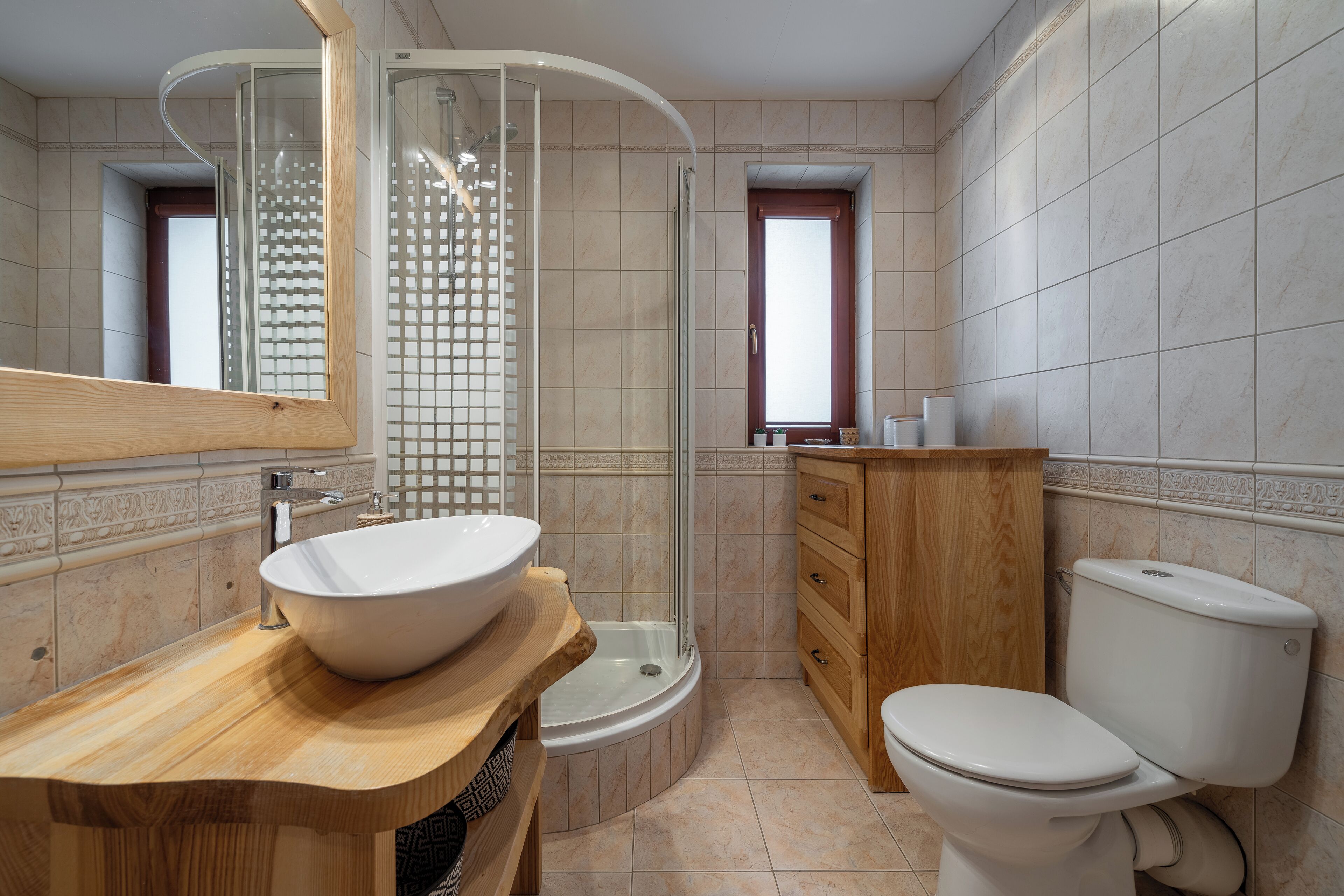 A modern bathroom with a wooden vanity, a large white sink, a glass-enclosed shower, and a toilet.