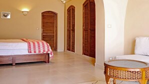A bedroom with a bed, a round wicker table, and wooden shutters on the wall.