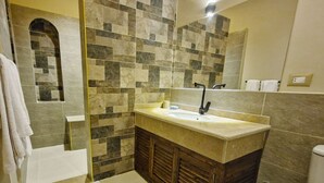 A bathroom with a stone tile shower, a sink with a wooden vanity, and a toilet.