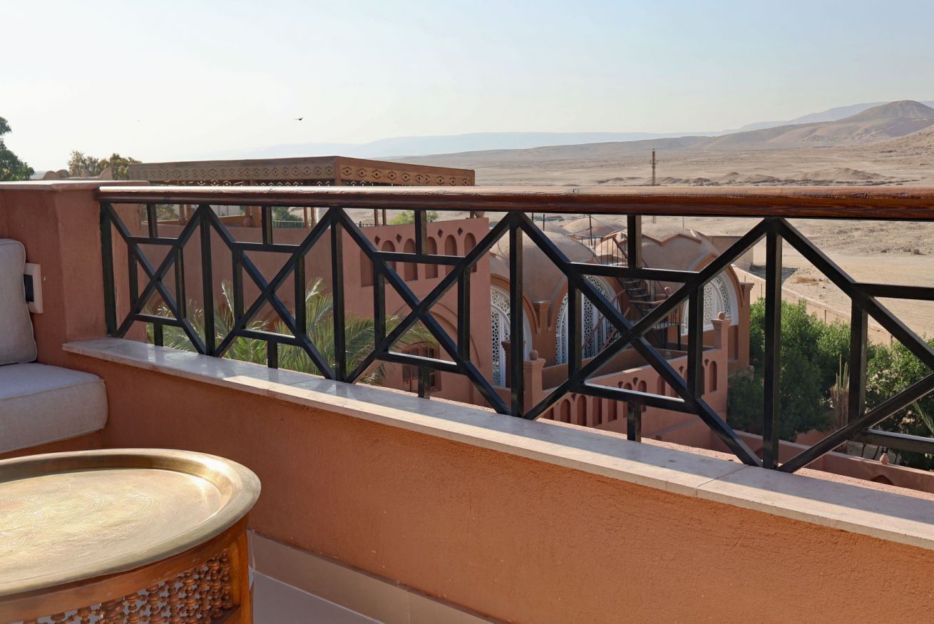 Un balcon doté d’une balustrade en fer forgé, d’un banc rembourré et d’une table ronde en bois.