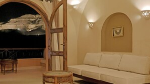 Una habitación acogedora con un sofá blanco, una mesa de madera y un gran ventanal de arco que da a un paisaje montañoso.