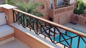 Un balcón con piscina, palmeras y un edificio con arcos.