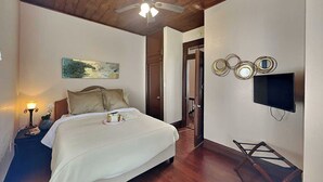 A hotel room with a bed, a television, a painting, and a ceiling fan. - The Magalena by Ryson Vacation Rentals (Galveston)