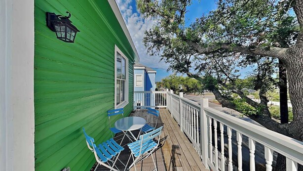 A green building with a wooden deck, blue chairs, and a white railing. - The Magalena by Ryson Vacation Rentals (Galveston)