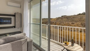 Ein Balkon mit Glastür, ein kleiner Tisch mit Flasche und Obst, sowie ein Fernseher an der Wand.