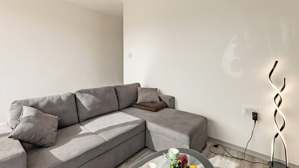 Ein modernes Wohnzimmer mit einem grauen Ecksofa, einem runden Couchtisch mit Früchten und einer außergewöhnlichen spiralförmigen Leuchte.