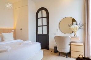 A hotel room with a bed, a desk with a mirror, a chair, and a door.