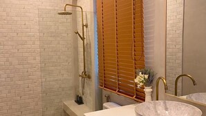 Un baño moderno con cabina de ducha de vidrio, inodoro y tocador con un lavabo redondo grande y un espejo.
