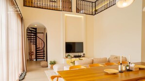 Un comedor amplio con una mesa y sillas de madera, un televisor en la pared y una escalera que sube a un nivel superior.