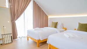 Habitación de hotel con dos camas de madera, cortinas color crema y un ventanal grande.