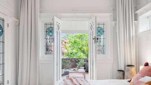 A bedroom with a bed, a window with curtains, and a view of an outdoor patio. - Five Dock Family Home With Pool & Parking! (Five Dock)