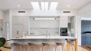 A modern kitchen with a central island, bar stools, and a large window. - Five Dock Family Home With Pool & Parking! (Five Dock)