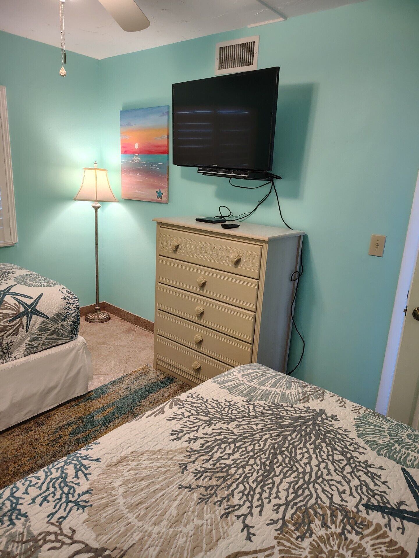 Un dormitorio con cama, cómoda, televisor y un cuadro en la pared.