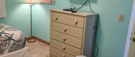 Un dormitorio con cama, cómoda, televisor y un cuadro en la pared.