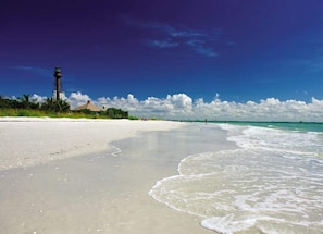 A beach with a lighthouse, clear skies, and calm waters.