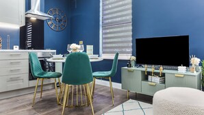 Ett modernt kök med turkosa stolar, en stor tv-skärm och ett fönster med persienner.