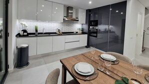 A modern kitchen with white cabinets, a black refrigerator, and a wooden dining table set for two.
