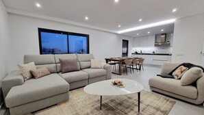 A modern living room with a grey sectional sofa, a round coffee table, and a dining area with a wooden table and chairs.