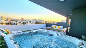 A rooftop terrace with a hot tub, outdoor seating, and a city view.
