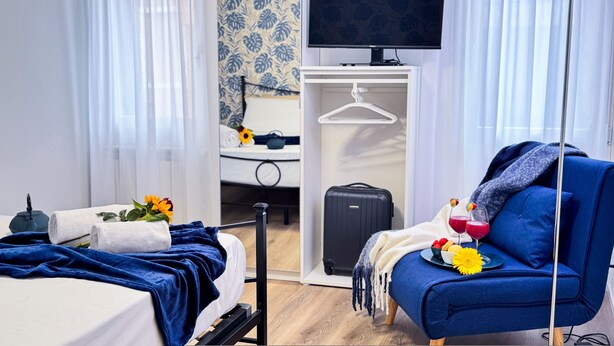 Una habitación de hotel con una cama, un sofá azul, un televisor, un armario y una maleta.