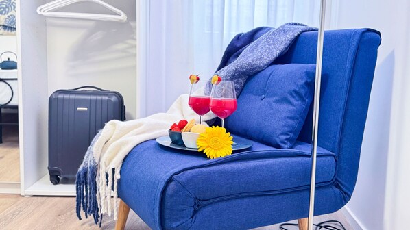 A blue armchair with a blanket, a tray with snacks and a flower, and a suitcase in a room with a white wall and a door.
