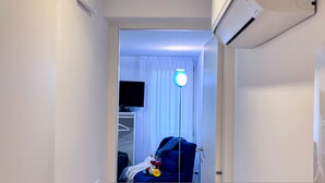 Habitación de hotel con cama, mesita de noche con lámpara, televisor montado en la pared y ventana con cortinas.