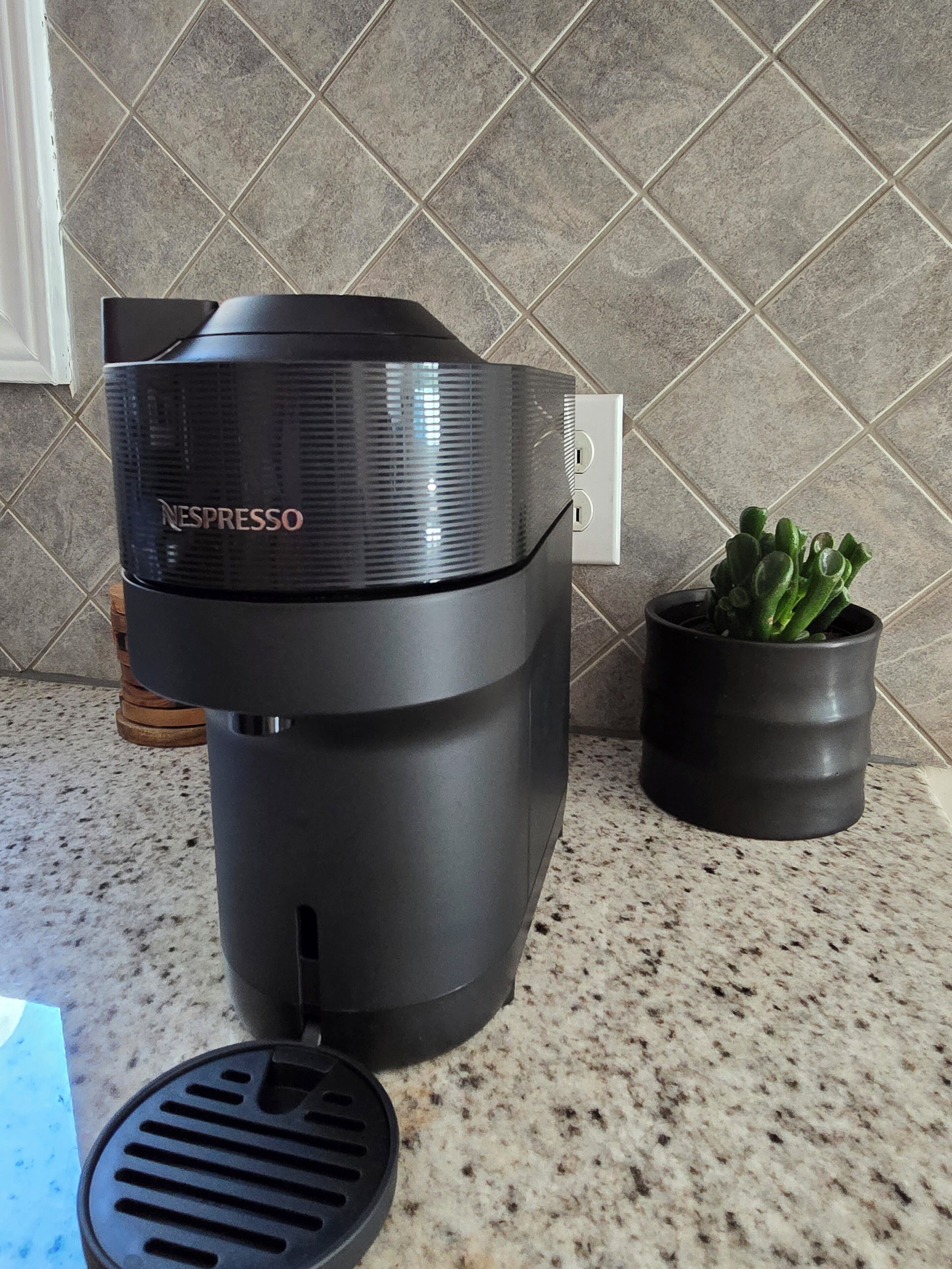 A Nespresso coffee machine on a kitchen counter with a potted plant beside it.