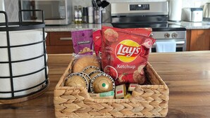 A kitchen with wooden cabinets, a microwave, and a stove. There is a basket with bread, a bag of Lay's chips, and a bottle of Kirkland water.