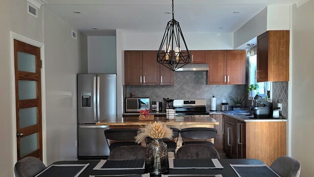 A modern kitchen with stainless steel appliances, wooden cabinets, and a dining area with a black table and chairs.
