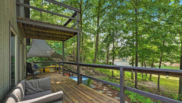 A wooden deck with a sofa and a table, overlooking a grassy area and a body of water. - Waterfront Beaver Lake Cabin Retreat (Rogers)