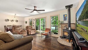 A spacious living room with a fireplace, comfortable seating, and large windows offering a view of the outdoors. - Waterfront Beaver Lake Cabin Retreat (Rogers)