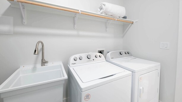 Een wasserij met een wasbak, twee witte Whirlpool wasmachines en een houten plank met een opgerolde handdoek.
