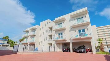 A multi-story residential building with balconies, a gated entrance, and a parking area.