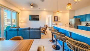 A modern living space with a sofa, dining table, bar stools, and a kitchen area with blue cabinets.