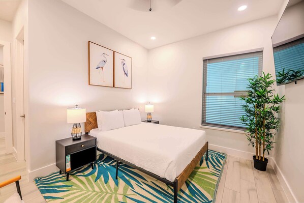 Un dormitorio moderno con cama, mesitas de noche, lámpara, ventana con persianas y una planta en maceta.
