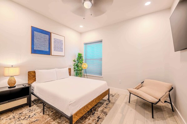 A bedroom with a bed, bedside table, lamp, and a chair.