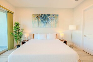 Une chambre d’hôtel avec un grand lit, deux tables de chevet avec des lampes, une lampe sur pied, une grande peinture abstraite au mur et une plante en pot.