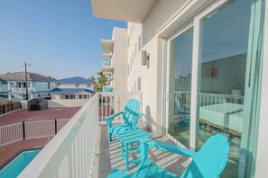 A balcony with a pool, blue Adirondack chairs, and a glass door leading to a patio area. - Surfside Sanctuary (South Padre Island)