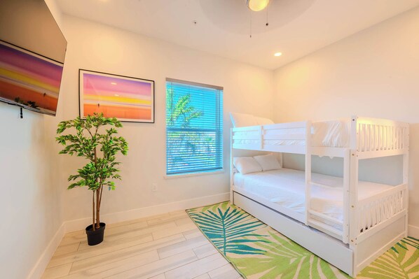Une chambre avec un lit superposé, une plante en pot et deux tableaux encadrés accrochés au mur.