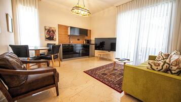 Una sala moderna con sofá, sillones, una mesa de centro, televisor, área de cocina y mesa de comedor.