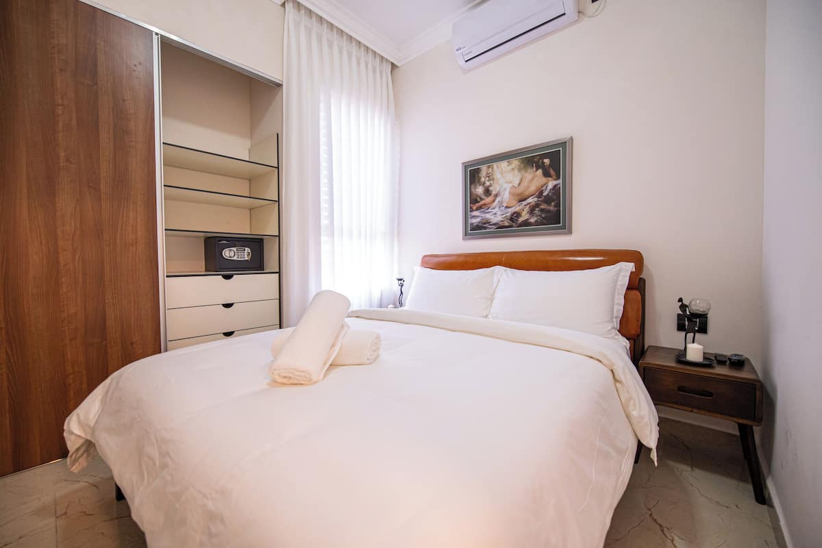 A neatly made bed with a rolled towel, a bedside table with a lamp, and a painting on the wall.